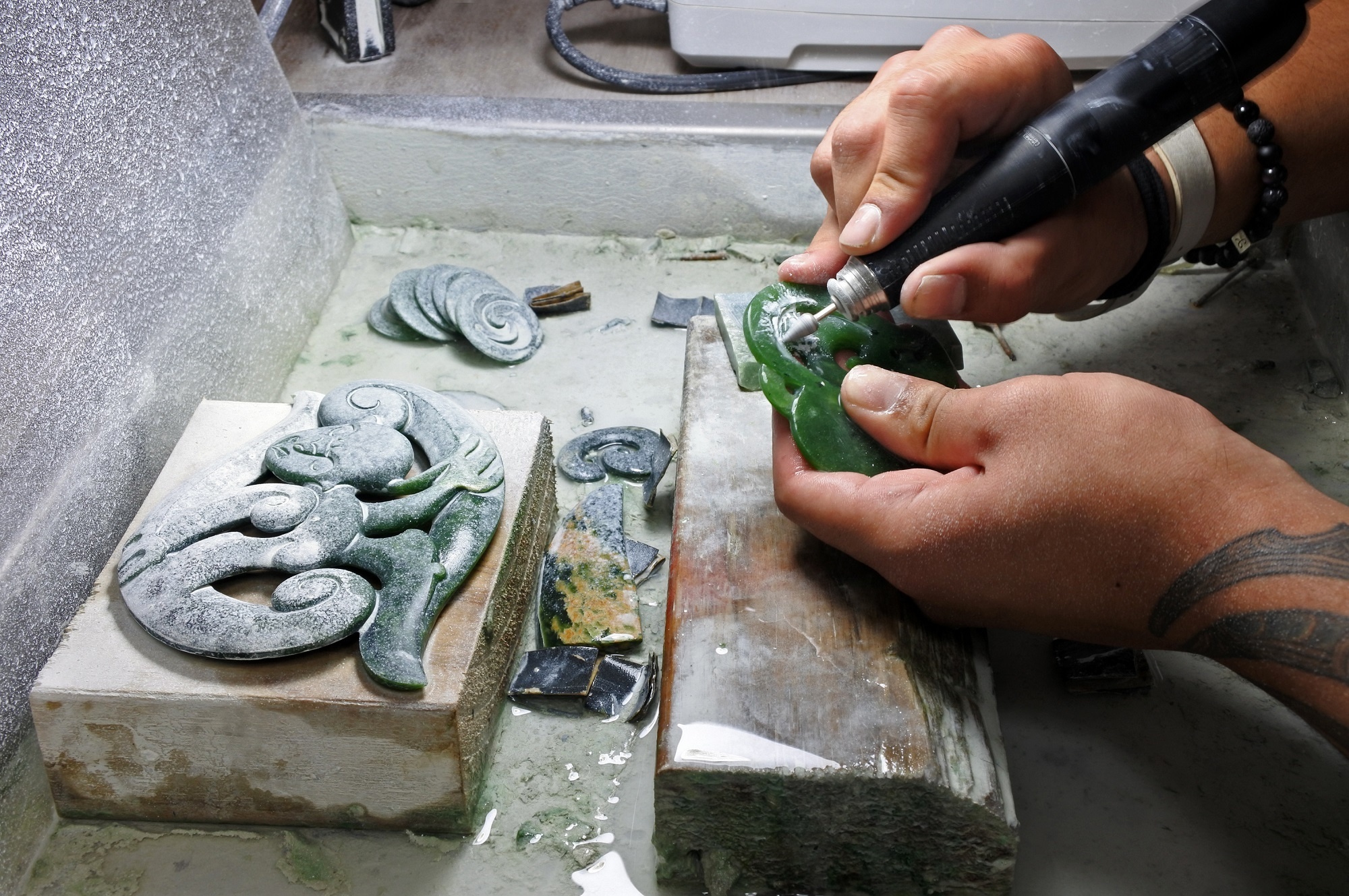 des mains en train de façonner une pierre de jade en forme moarie
